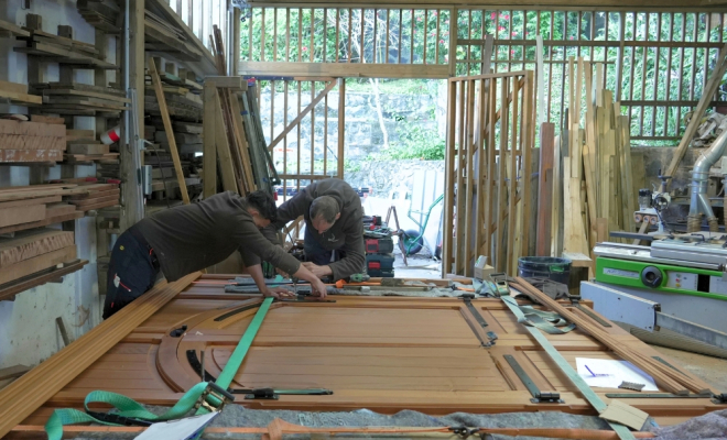 finition ferrure de la porte en Moabi, dans l'atelier de menuiserie avec deux ouvriers
